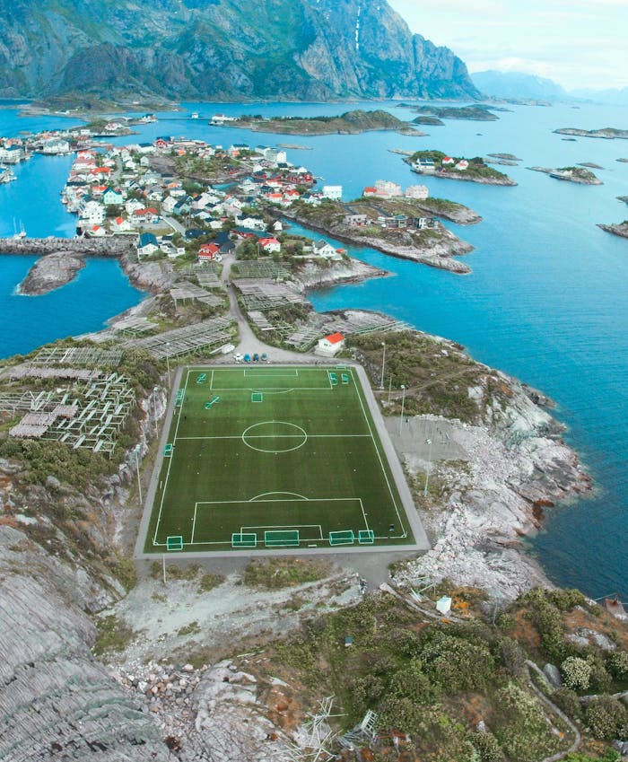 Home A breathtaking aerial view of a soccer field in Lofoten Islands, Vågan, Norway surrounded by stunning seascape and mountains.
