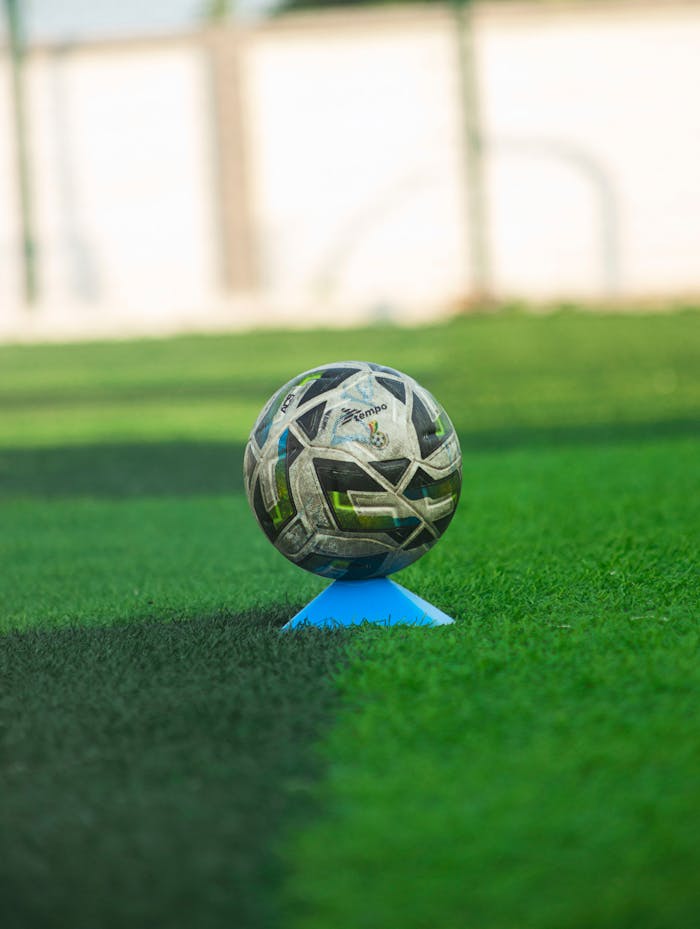 Home Soccer ball resting on teal cone on lush green field. Perfect for sports themes.