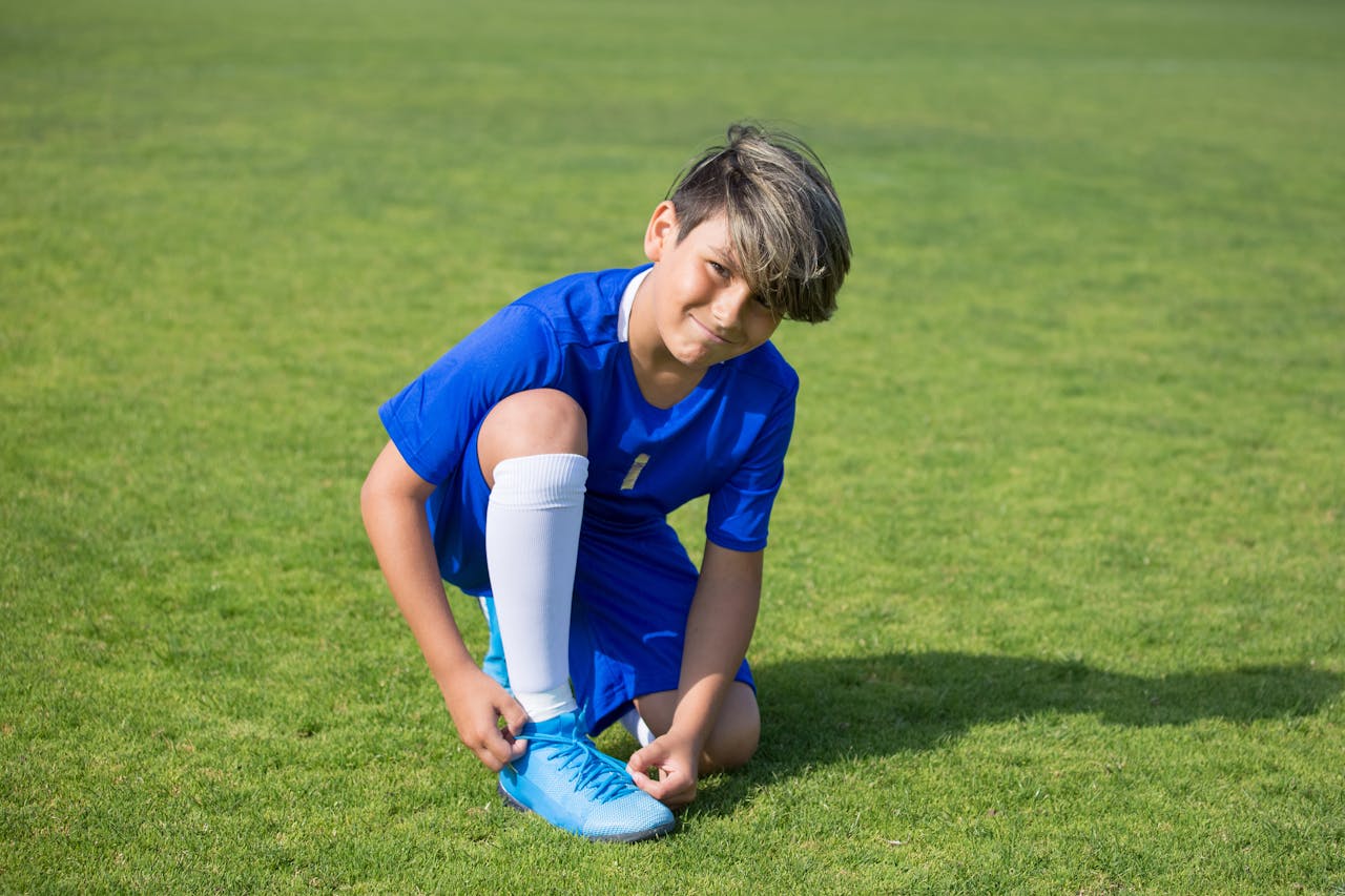 A young soccer player ties his shoelaces on a sunny day outdoors, preparing for a game.